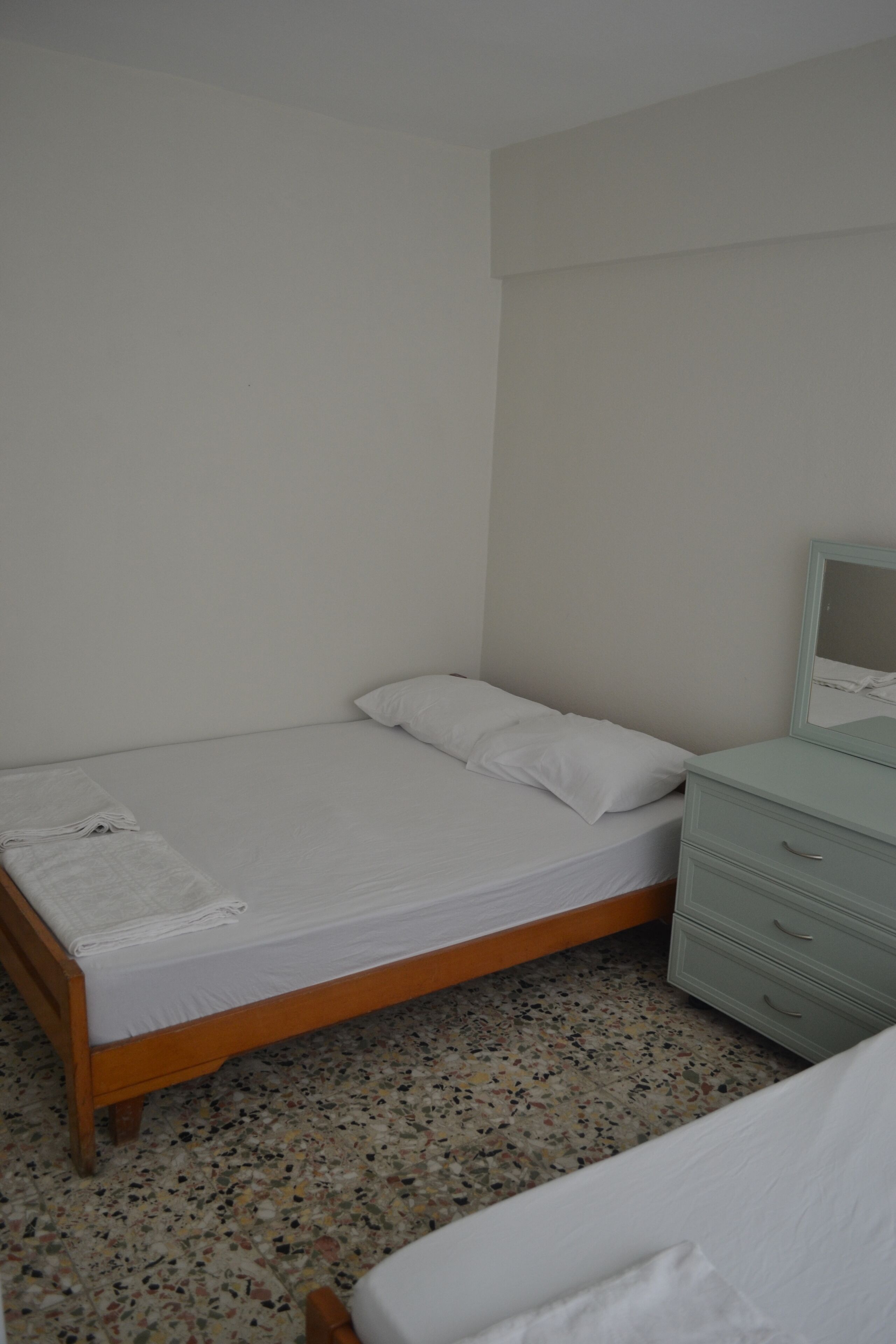A small, clean room with a single bed, a nightstand, and a mirror.