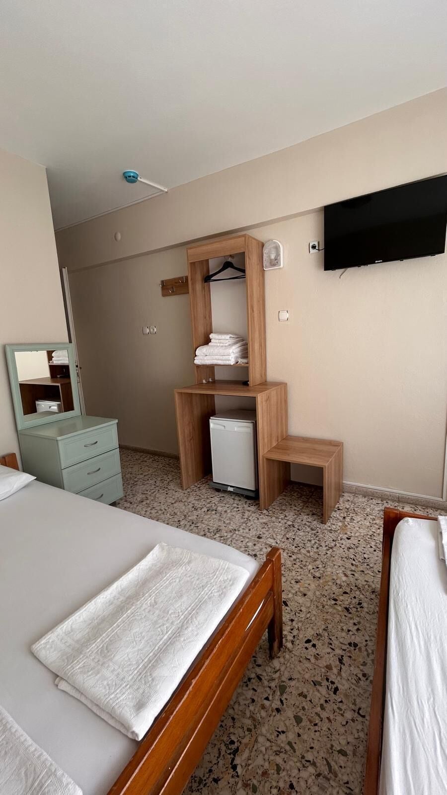 A hotel room with two beds, a wardrobe, a desk, a chair, a television, and a small refrigerator.