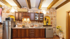 Una cucina con pareti in pietra, mobili in legno, frigorifero in acciaio inossidabile, lavastoviglie e lavello.