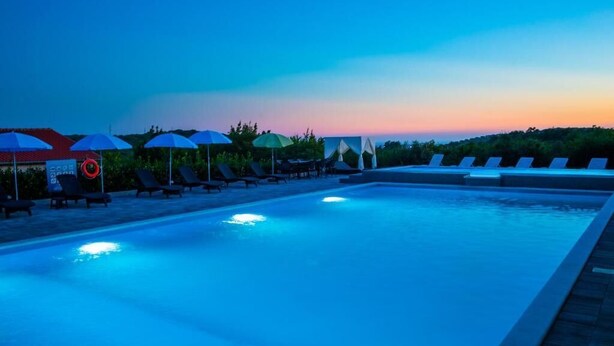 Una piscina con lettini e ombrelloni, immersa nel verde.