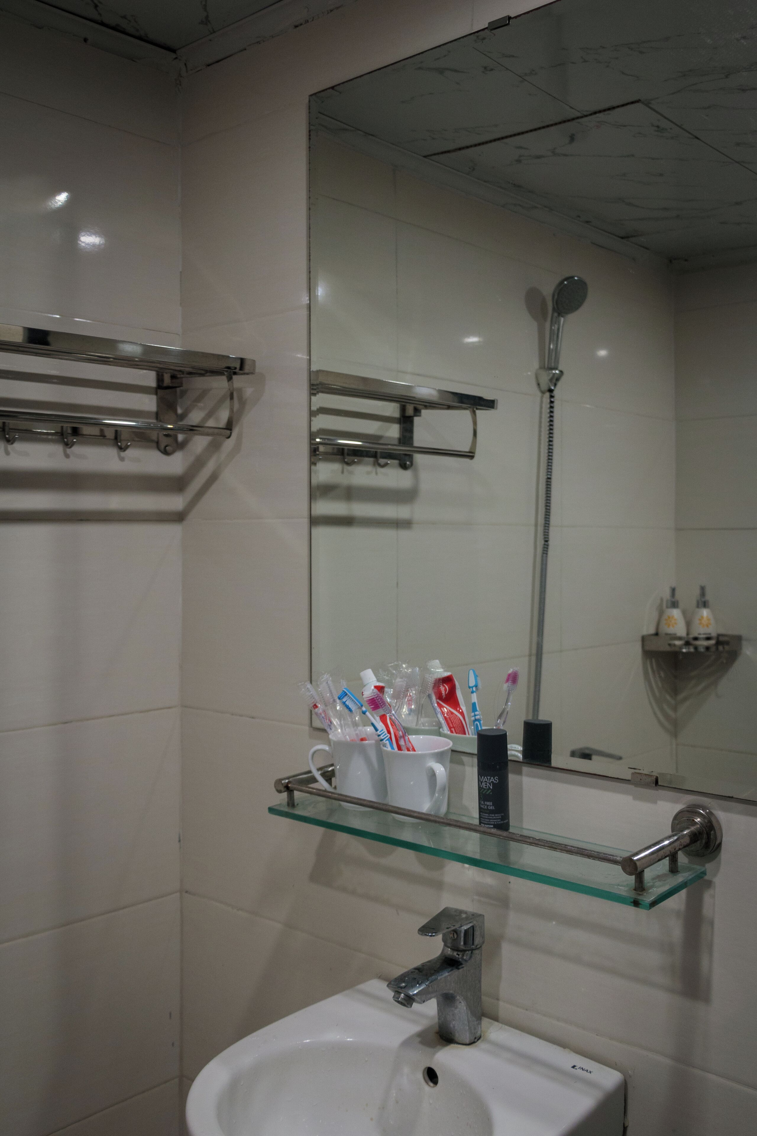 A bathroom with a white sink, a glass shelf with toiletries, a mirror, and a shower.