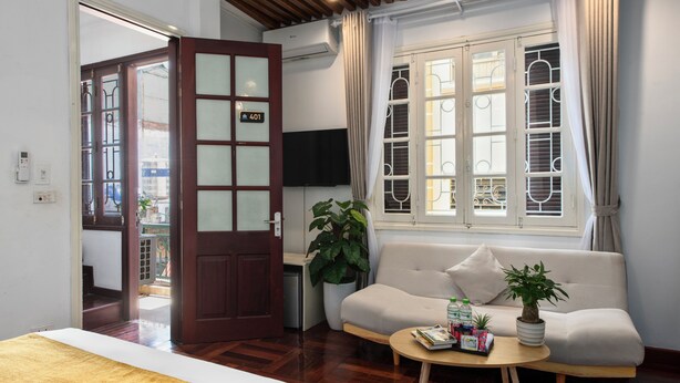 A hotel room with a bed, a sofa, a small table with magazines, a potted plant, and a TV. - Hanoi Family Homestay (Hanoi)