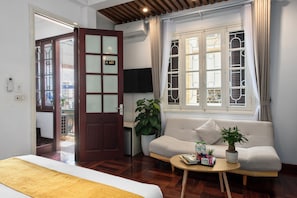 Une chambre d’hôtel avec un lit, un canapé, une petite table avec des magazines, une plante en pot et un téléviseur.