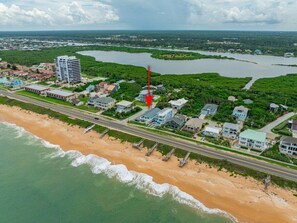 Vista aérea de uma cidade costeira com uma praia, um rio e uma estrada que leva a um conjunto de casas.