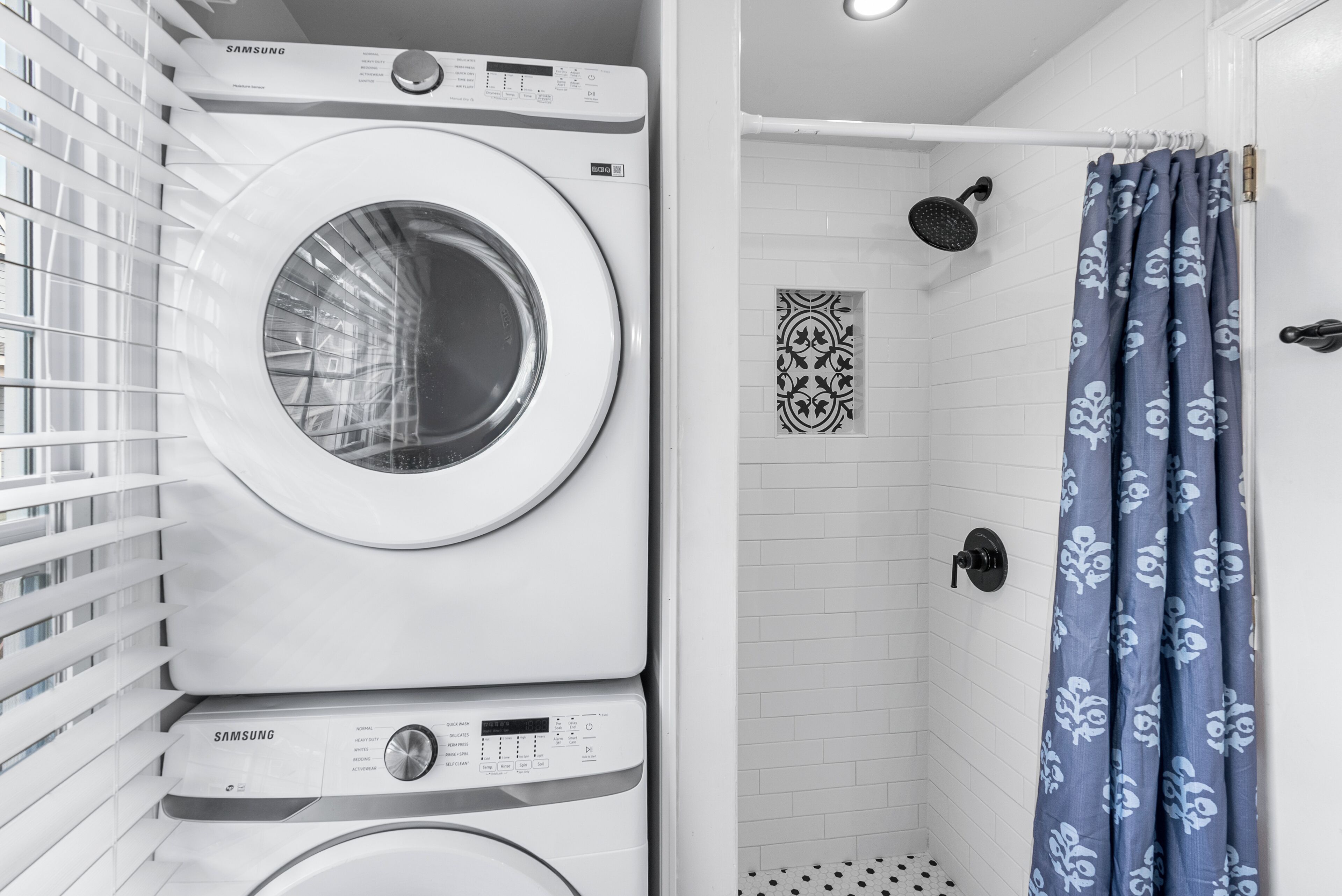 A laundry area with stacked washing machines and a shower with a patterned curtain.