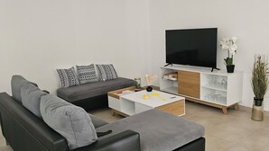 A modern living room with a black sofa, a white coffee table, and a TV on a white cabinet. - Lower villa F3 (Alata)