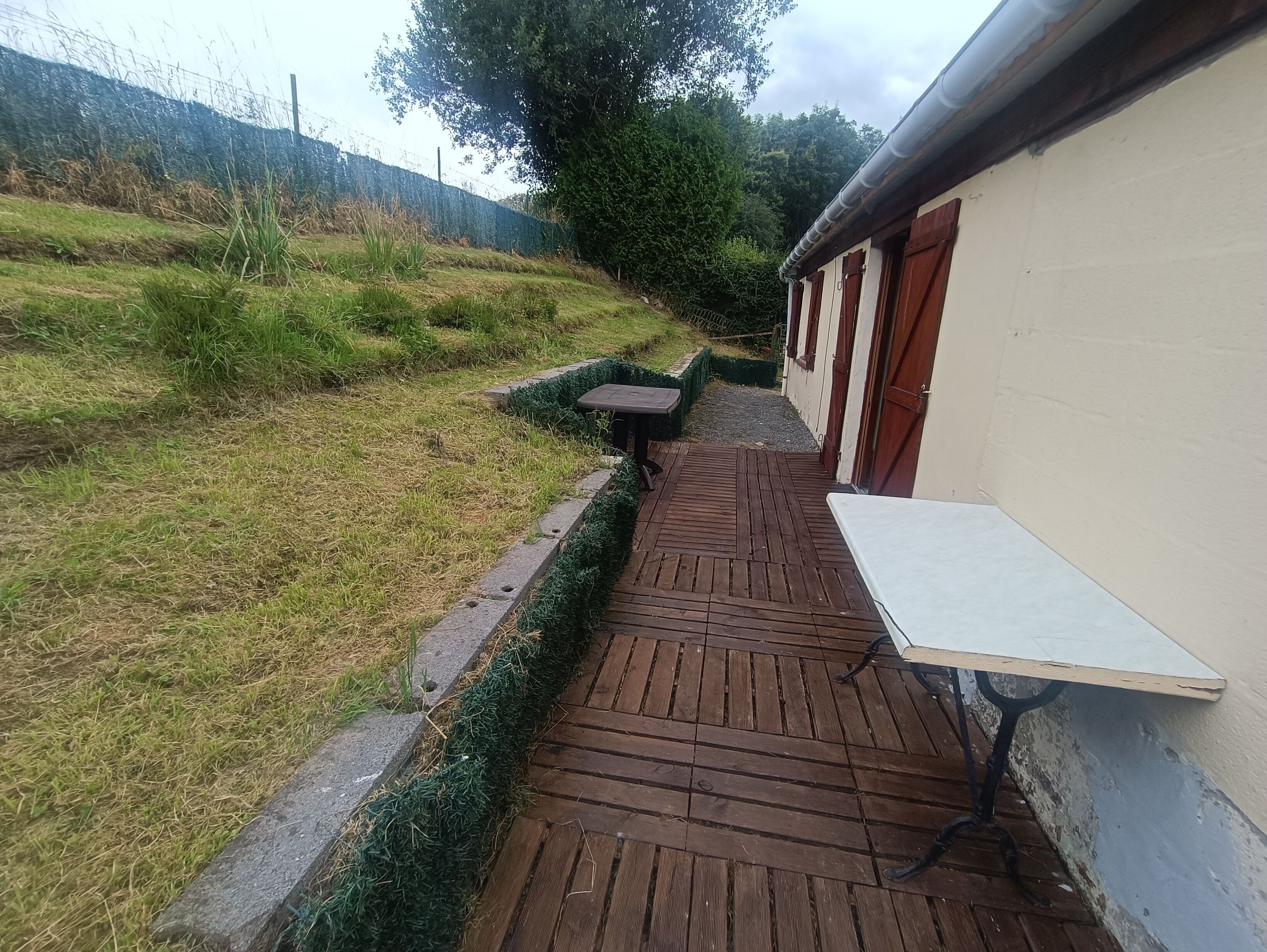 Een smal houten pad dat leidt naar een gebouw met een kleine tafel en bank.