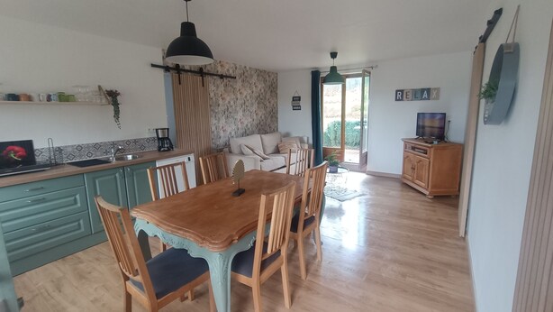 A spacious kitchen with wooden cabinets, a dining table with chairs, a sofa, and a TV in a living area. - Le chalet du Lilas (Liessies)