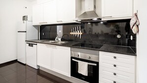 A modern kitchen with white cabinets, a black countertop, stainless steel appliances, and a black backsplash.