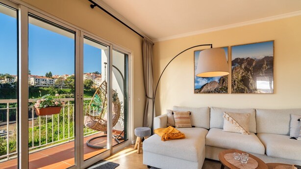 A modern living room with a sofa, a coffee table, and a hanging chair on a balcony with a city view.