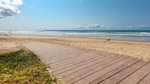 Un paseo marítimo de madera que conduce a una playa arenosa con vistas al océano.