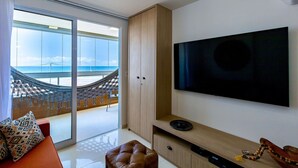 Un moderno salón con un televisor de pantalla plana grande, una zona de estar acolchada y vistas a un puente y una playa a través de un ventanal.