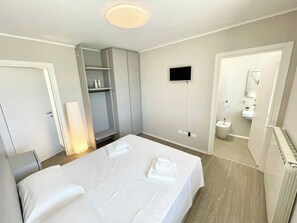 Een moderne hotelkamer met een bed, nachtkastjes, een kledingkast, een televisie en een badkamer met toilet en wastafel.