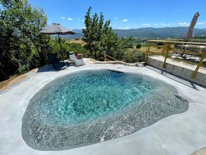 Una vasca idromassaggio circondata da un solarium con poltrone relax, un pergolato in legno e vista sulla campagna.