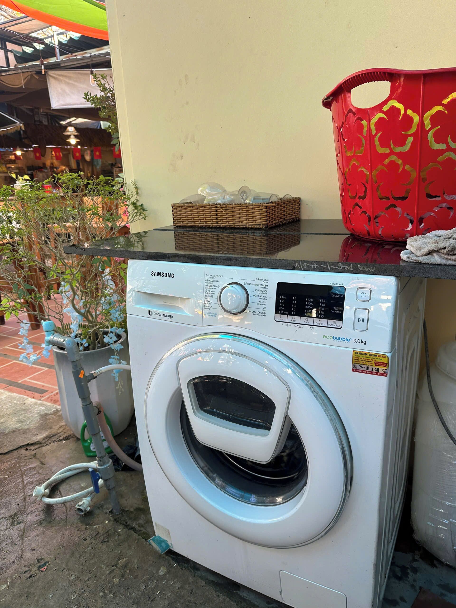 A Samsung digital inverter washing machine with a control panel, a basket, and a red container on top.