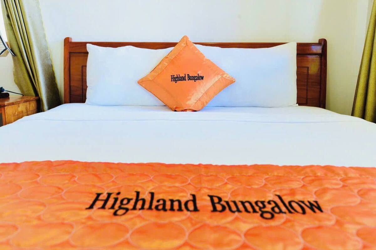 A bed with a white mattress and pillows, a wooden headboard, and a blanket with "Highland Bungalow" text.