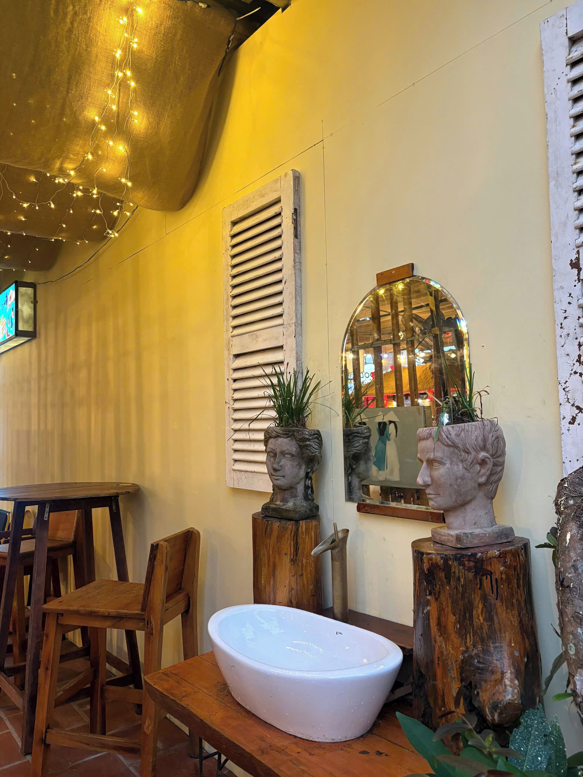 A cozy dining area with a wooden table, chairs, a white bowl, and decorative busts on wooden stands.