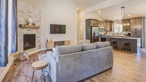Een moderne woonkamer met een open haard, een grijze bank en een keuken met roestvrijstalen apparatuur.