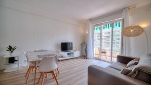 Una sala de estar moderna con comedor, televisor de pantalla plana, sofá y un amplio ventanal corredera que da a un balcón.