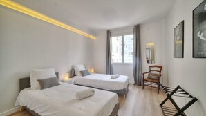 Habitación de hotel con dos camas, un escritorio, una silla, un espejo y una ventana con cortinas.