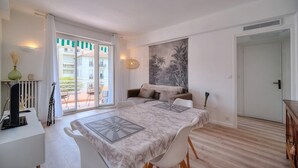Habitación de hotel con una cama grande, un sofá, una mesa de comedor y vistas al balcón exterior.