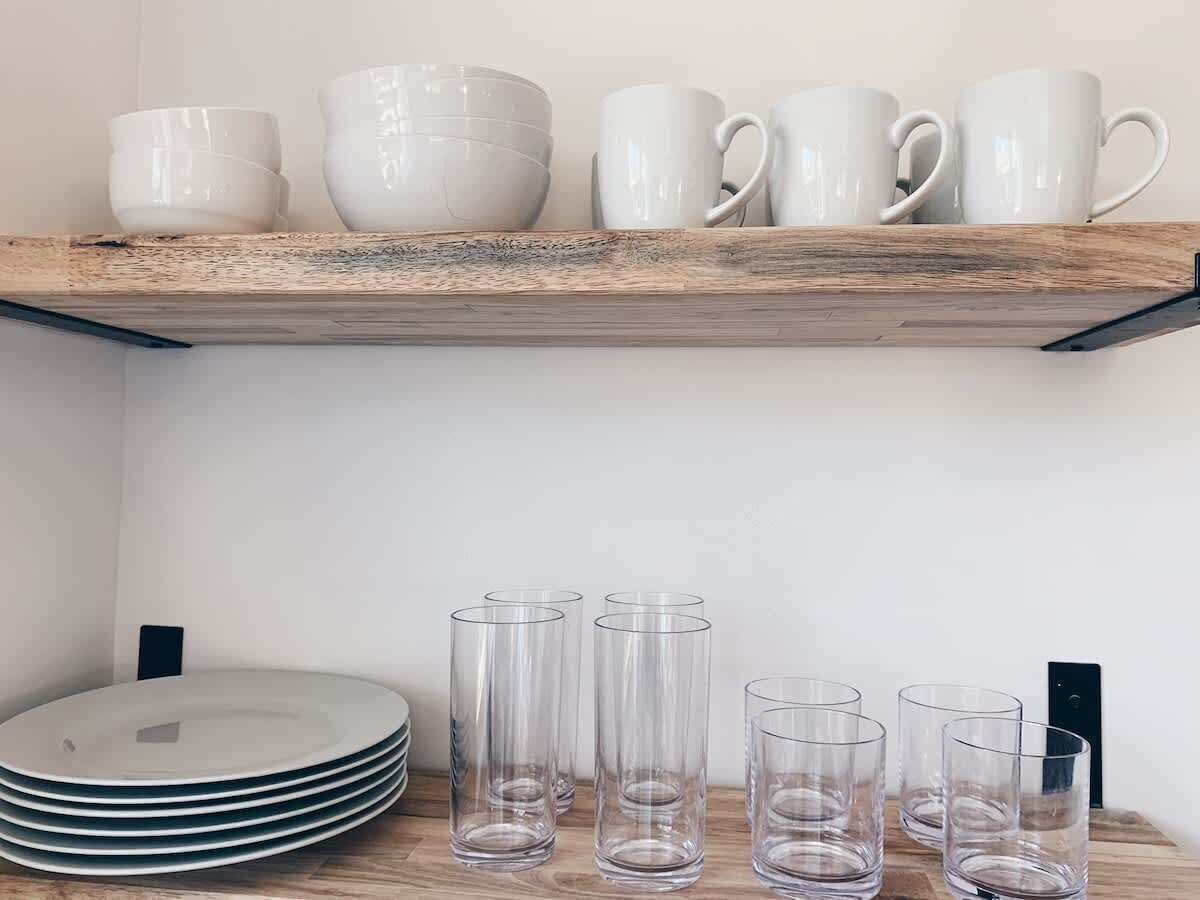 A shelf with white bowls and mugs, and below it, stacked plates and clear glasses.