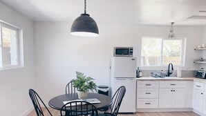 Eine moderne Küche mit weißen Schränken, einer Mikrowelle und einem Spülbecken. Ein Esstisch mit Stühlen und ein Blumentopf sind ebenfalls vorhanden.