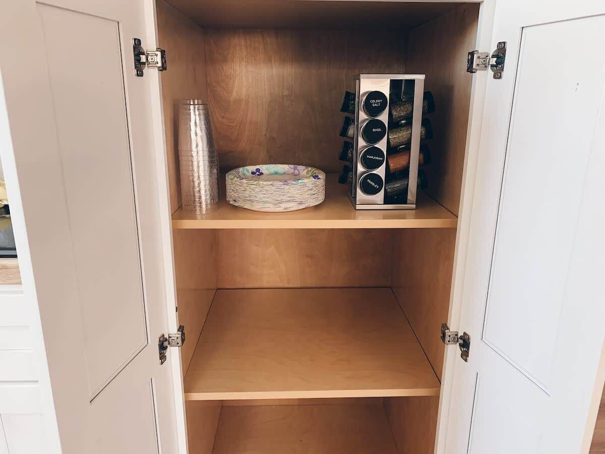 Un meuble en bois avec un étagère à épices sur l’étagère supérieure et un panier tressé sur l’étagère du milieu.