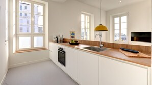 A modern kitchen with white cabinets, a wooden countertop, a built-in oven, a sink, and a yellow pendant light. - Upstays Harbor View 83m² Apartment Palais (Cannes)