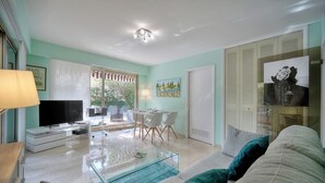A modern living room with a glass coffee table, a TV, and a dining area with chairs and a table. - Upstays Terrace Garden 44m² Apartment (Cannes)
