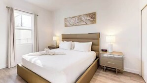Hotellihuone, jossa on suuri sänky, yöpöydät, seinälle ripustettu taideteos ja ikkuna, jossa on verhot.