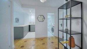 Une cuisine moderne dotée d’un îlot central, d’un miroir hexagonal et d’une étagère noire où sont disposés des objets décoratifs.