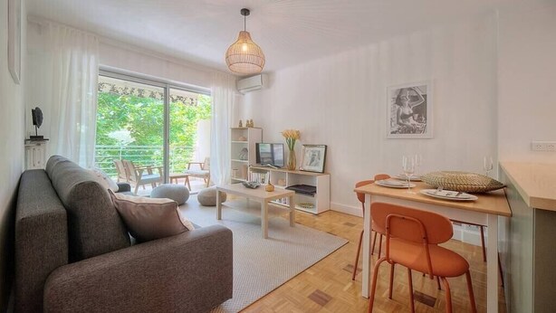 Un salon moderne comprenant un canapé, un coin repas avec une table et des chaises, un téléviseur et une grande fenêtre donnant sur un paysage verdoyant.