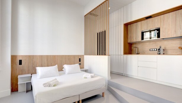 Une chambre d’hôtel moderne dotée d’un grand lit, d’une cloison en bois, d’une kitchenette avec un four à micro-ondes et d’un design épuré et minimaliste.