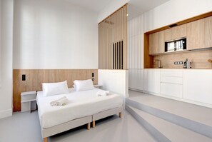 Une chambre d’hôtel moderne dotée d’un grand lit, d’une cloison en bois, d’une kitchenette avec un four à micro-ondes et d’un design épuré et minimaliste.