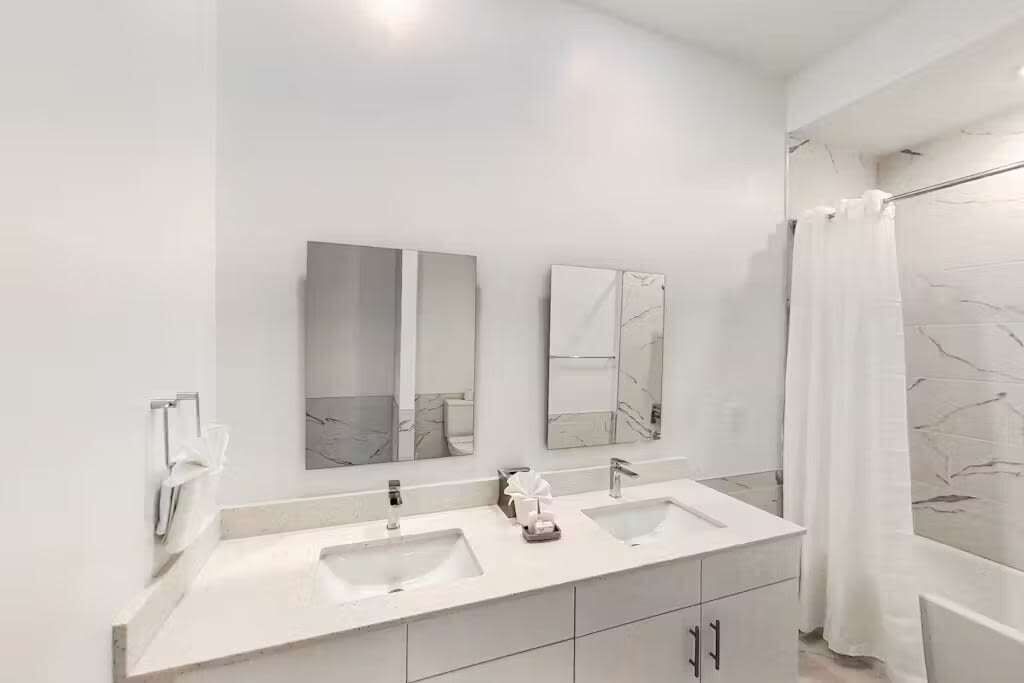 Une salle de bain moderne avec deux lavabos, un grand miroir et un rideau de douche.