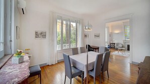A dining area with a table set for six, a large window with curtains, and a view of the outside. - Upstays Terrace Garden 100m² Villa Center (Cannes)