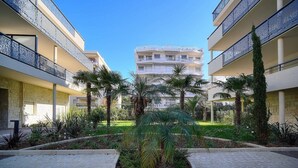 Ein Innenhof mit einer zentralen Palme, umgeben von einem Backsteinweg und begrenzt von zweistöckigen Gebäuden mit Balkonen.