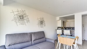 A modern living room with a grey sofa, a wooden dining table with chairs, and a kitchen in the background. - Upstays Croisette Terrace 35m² Apartment (Cannes)