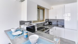 A modern kitchen with white cabinets, a built-in oven, a microwave, and a sink. - Upstays Croisette Terrace 35m² Apartment (Cannes)