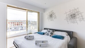A modern hotel room with a large bed, two pillows, and a view of the city through a large window. - Upstays Croisette Terrace 35m² Apartment (Cannes)