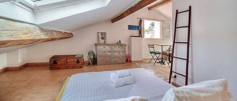 A bedroom with a skylight, a bed, a dresser, a fan, and a desk with a chair.