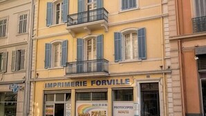 En gul bygning med flere balkoner og en butiksfacade med skiltet "IMPRIMERIE FORVILLE", samt synlige skilte for "KOPIER" og "HURTIGSERVICE".