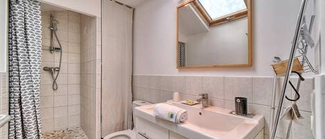 Et badeværelse med bruser, toilet, vask og spejl.