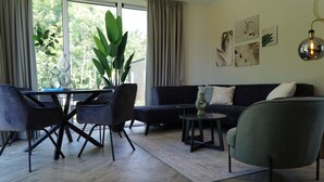 A modern living room with a dark sofa, a green armchair, and a dining area with black chairs and a glass table. - Europarcs Kagerplassen (Warmond)