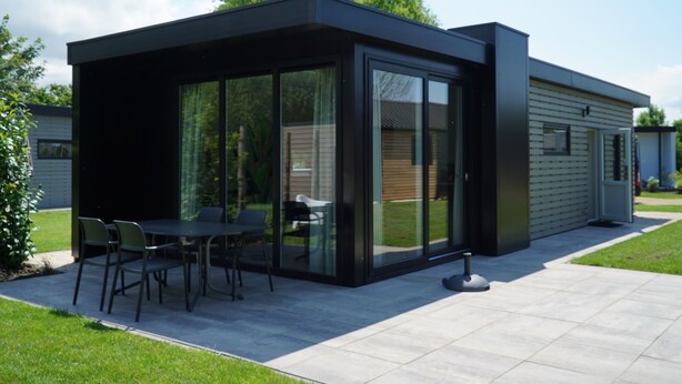 A modern house with a patio area featuring a table and chairs, large glass doors, and a well-maintained lawn. - Europarcs Kagerplassen (Warmond)