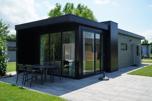 A modern house with a patio area featuring a table and chairs, large glass doors, and a well-maintained lawn. - Europarcs Kagerplassen (Warmond)