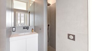 A modern bathroom with a white vanity, a large mirror, and a shower area. - Upstays Harbor View 45m² Apartment Palais (Cannes)