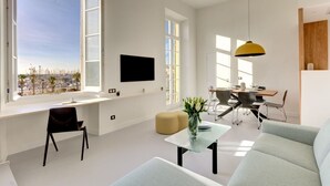 A modern living room with a large window, a flat-screen TV, a dining area, and a sofa. - Upstays Harbor View 45m² Apartment Palais (Cannes)