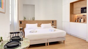 Ein modernes Hotelzimmer mit Bett, kleinem Esstisch, Tellern, Gläsern, einer Mikrowelle und einer Kaffeemaschine.